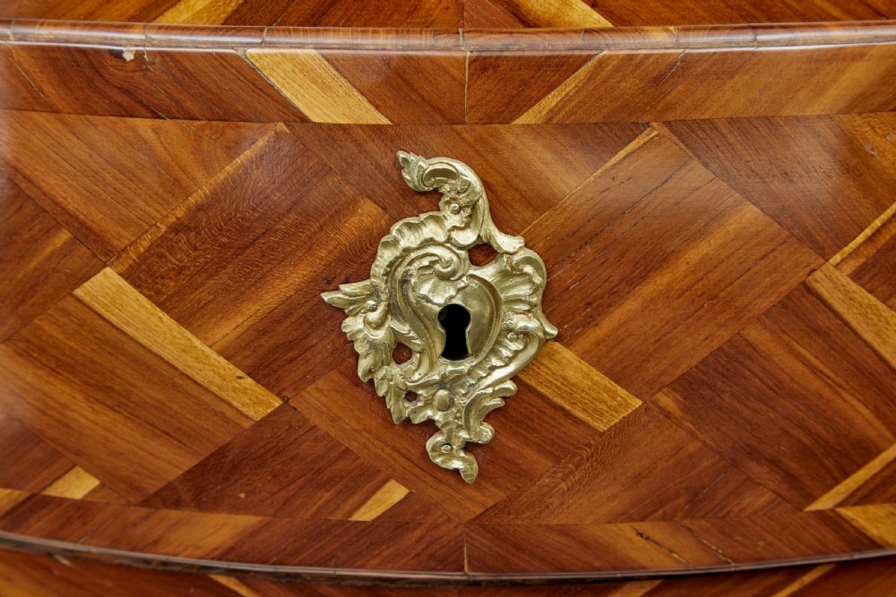 An early 18th-century Rococo bombe chest of drawers featuring geometric parquetry inlay in plumwood and three drawers with ornate brass handles. View IX