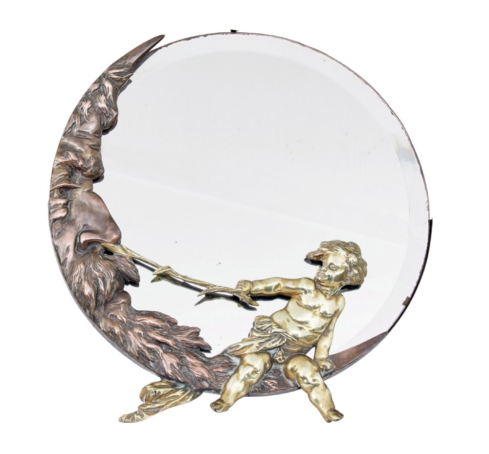A circular table mirror featuring a cast bronze crescent man-in-the-moon frame and a brass cherub seated along the bottom edge.