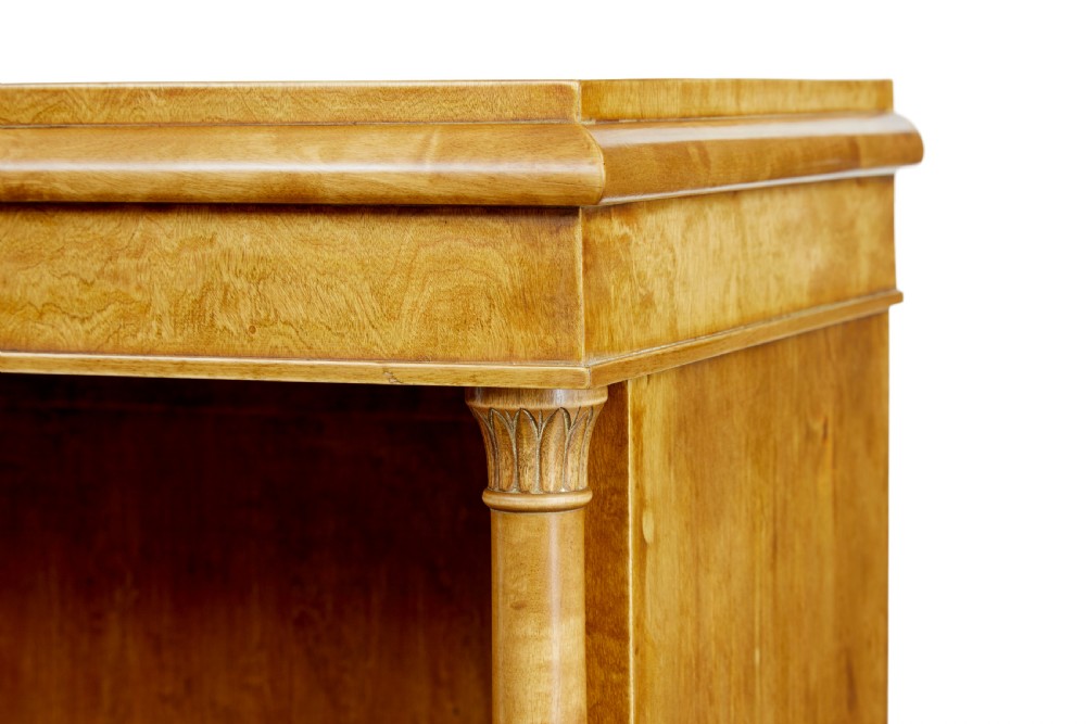 An early twentieth-century Empire Revival satin birch bookcase cabinet featuring open adjustable upper shelving and three lower panelled cupboard doors with a central carved drape motif. View IX