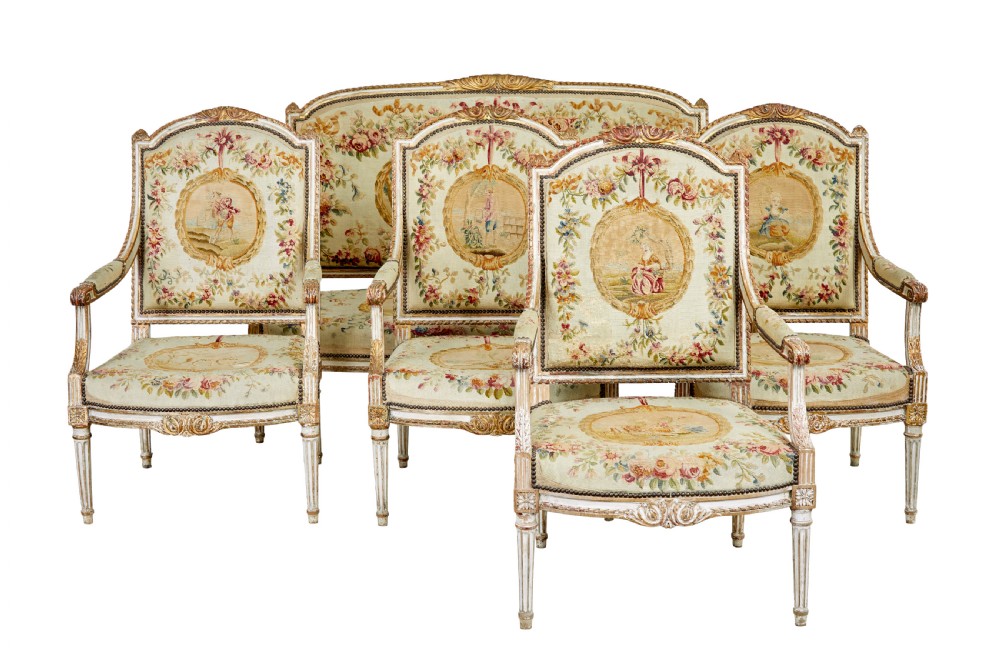 A five-piece French giltwood salon suite comprising four carved armchairs and a matching sofa, all upholstered in cream woven tapestry with floral and figurative medallions.