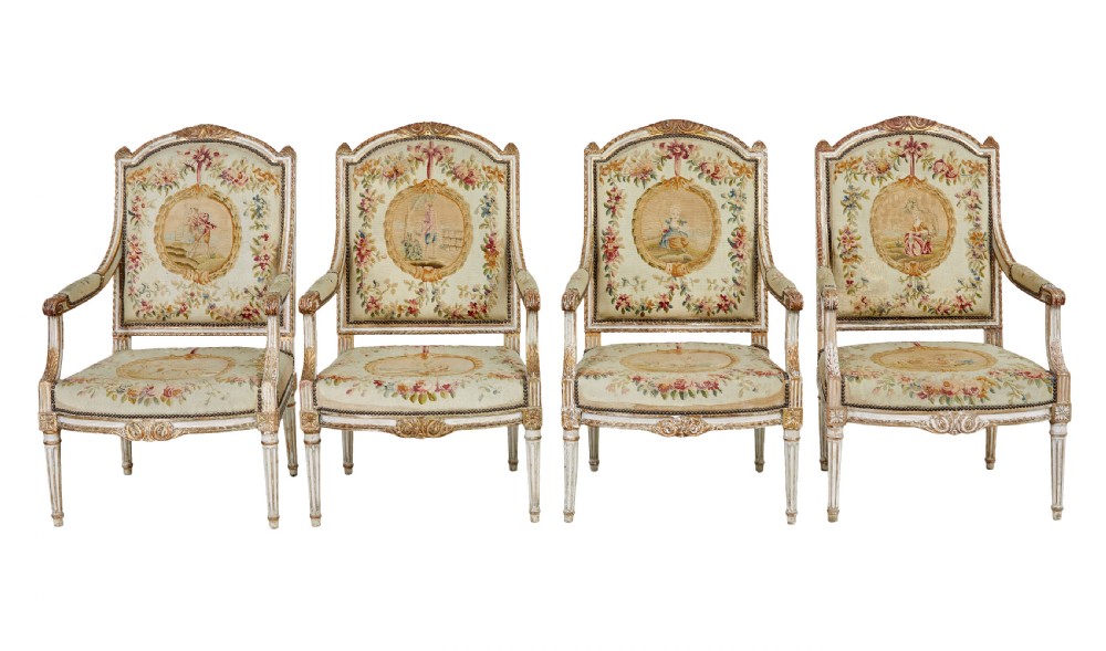 A five-piece French giltwood salon suite comprising four carved armchairs and a matching sofa, all upholstered in cream woven tapestry with floral and figurative medallions. View II