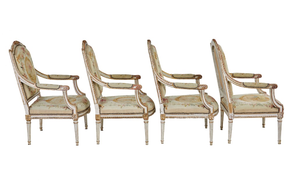 A five-piece French giltwood salon suite comprising four carved armchairs and a matching sofa, all upholstered in cream woven tapestry with floral and figurative medallions. View IV