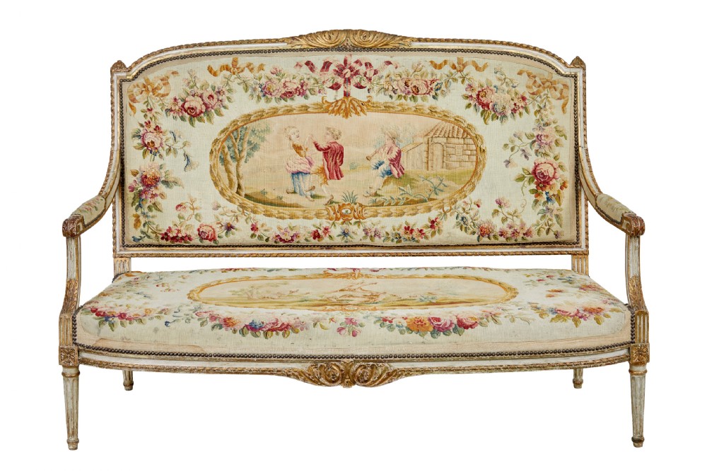 A five-piece French giltwood salon suite comprising four carved armchairs and a matching sofa, all upholstered in cream woven tapestry with floral and figurative medallions. View XVI