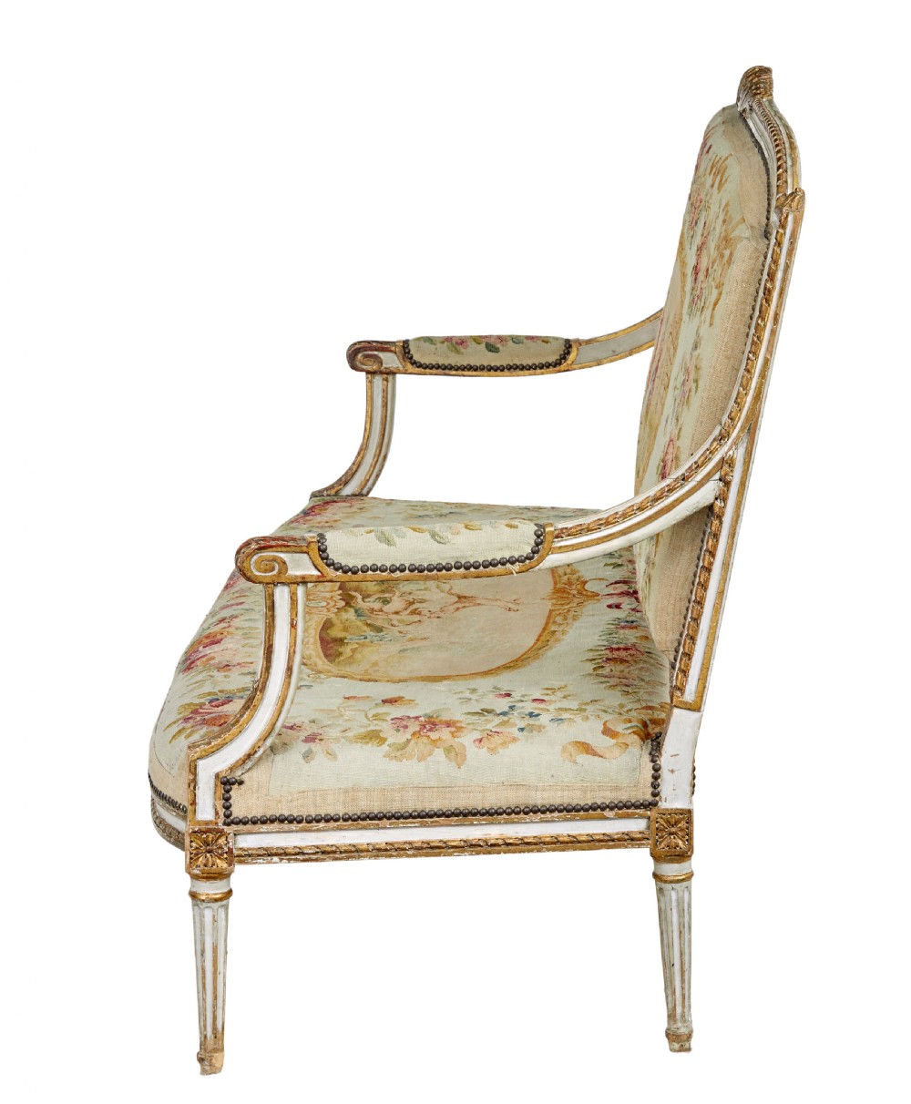 A five-piece French giltwood salon suite comprising four carved armchairs and a matching sofa, all upholstered in cream woven tapestry with floral and figurative medallions. View XVII
