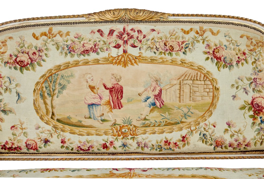 A five-piece French giltwood salon suite comprising four carved armchairs and a matching sofa, all upholstered in cream woven tapestry with floral and figurative medallions. View XX