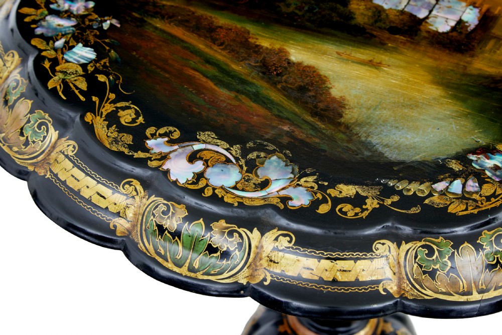 A 19th-century black lacquered papier-mache tilt-top table with a scalloped edge, hand-painted landscape, mother-of-pearl inlay, and gilded floral scrollwork on a turned pedestal. View IV