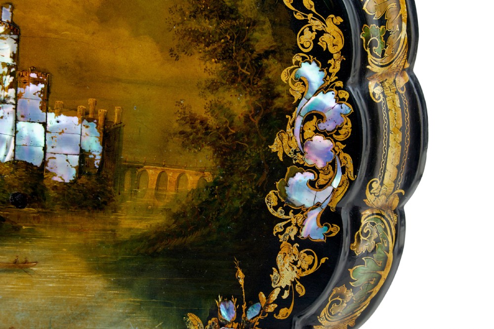 A 19th-century black lacquered papier-mache tilt-top table with a scalloped edge, hand-painted landscape, mother-of-pearl inlay, and gilded floral scrollwork on a turned pedestal. View VII