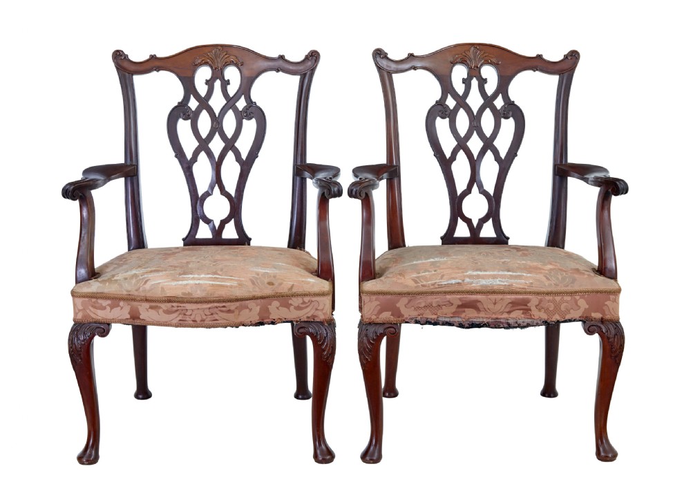 A pair of early 20th-century Chippendale Revival mahogany armchairs featuring carved pierced splat backs, serpentine top rails, curved arms, and cabriole legs.