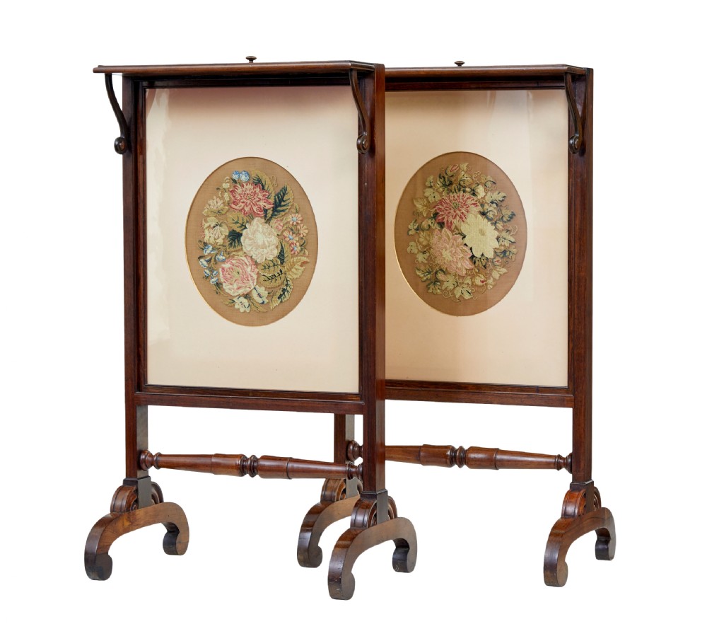 A pair of Regency palisander fire screens with turned stretchers, splayed scroll feet, and central oval floral needlepoint panels.