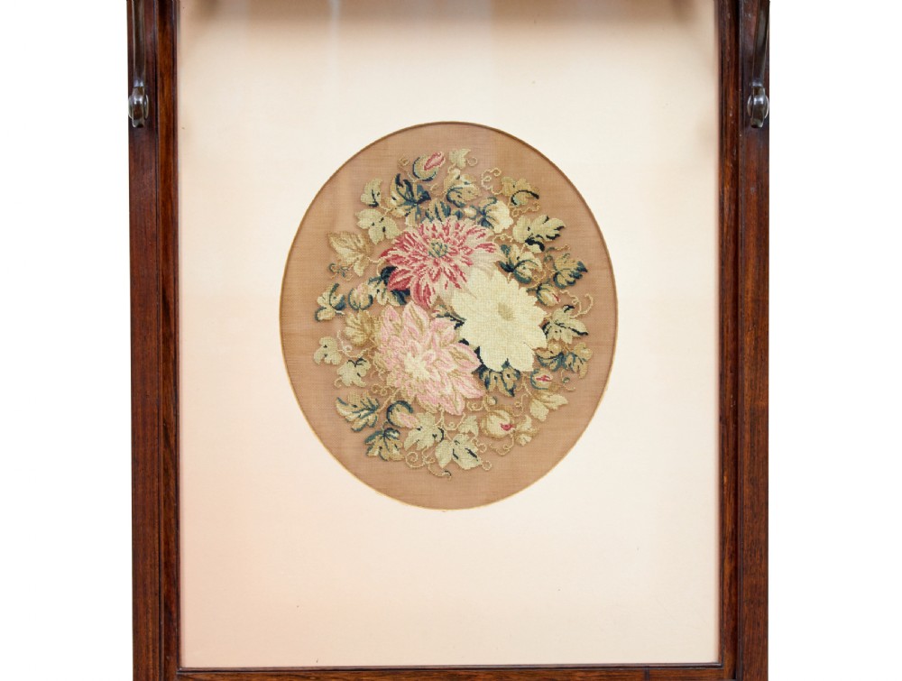 A pair of Regency palisander fire screens with turned stretchers, splayed scroll feet, and central oval floral needlepoint panels. View X