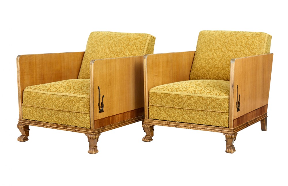 A pair of Art Deco lounge armchairs featuring light birch and elm veneered side panels, golden yellow patterned upholstery, and carved wooden feet.
