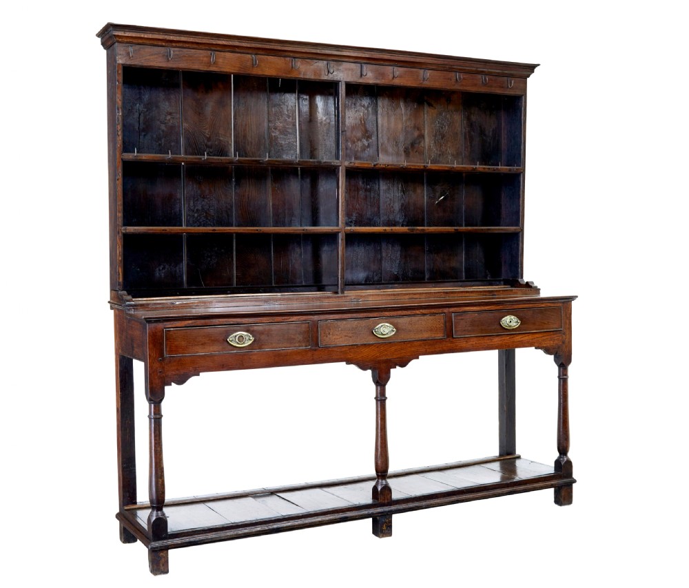 An early nineteenth-century Welsh oak dresser featuring a tall open plate rack with hooks above a three-drawer base supported by turned front legs and a lower pot board.