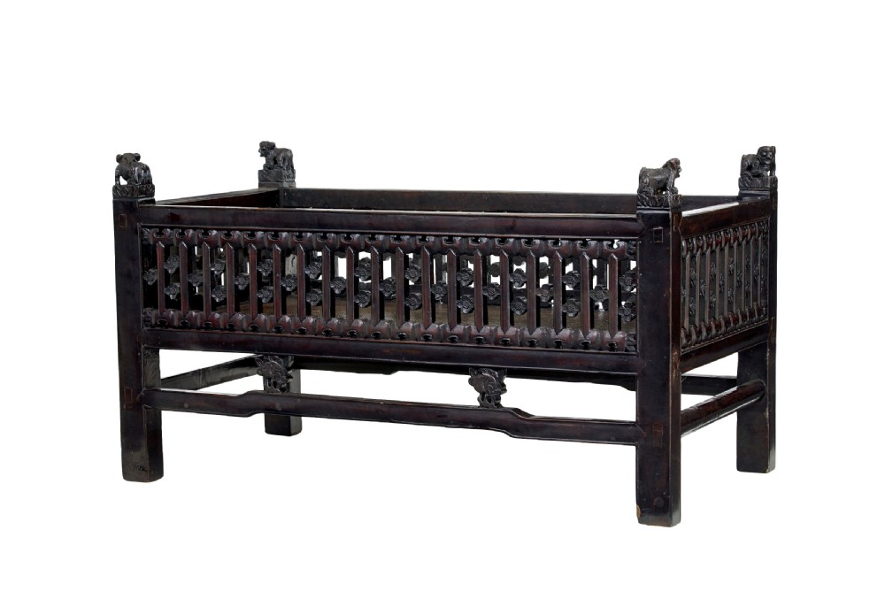 A 19th-century dark lacquered Chinese childs bed featuring carved lattice sides and guardian lion corner finials.