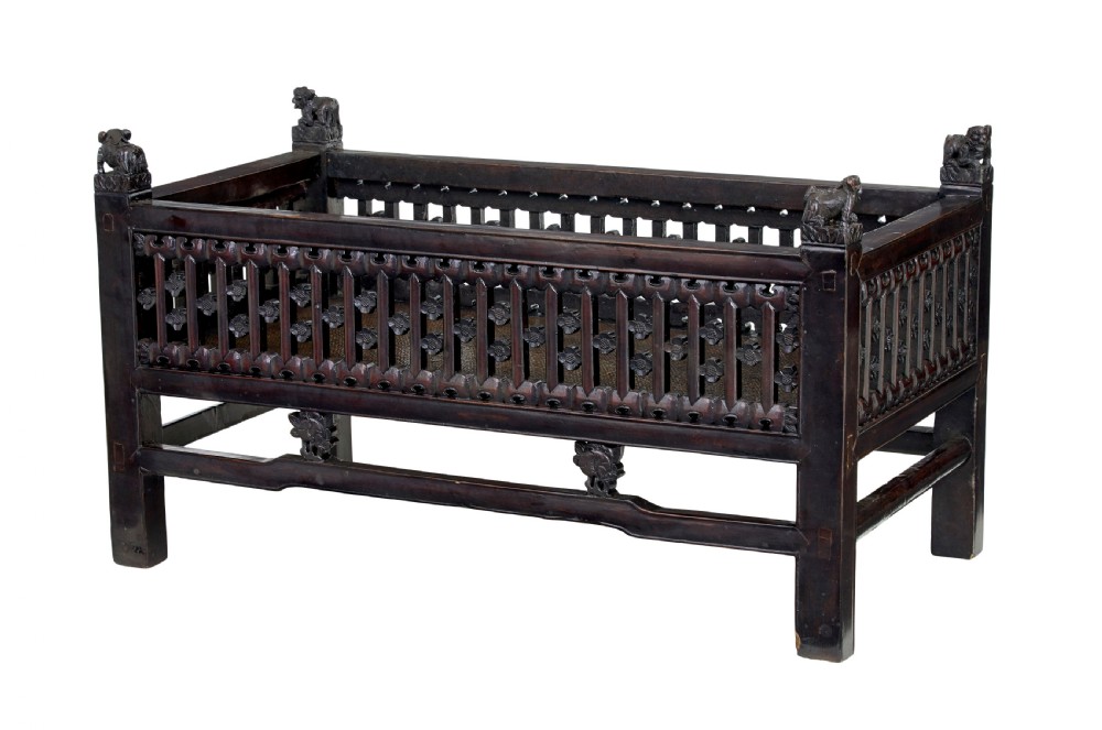 A 19th-century dark lacquered Chinese childs bed featuring carved lattice sides and guardian lion corner finials. View II