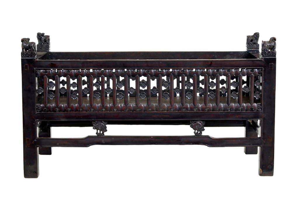 A 19th-century dark lacquered Chinese childs bed featuring carved lattice sides and guardian lion corner finials. View III