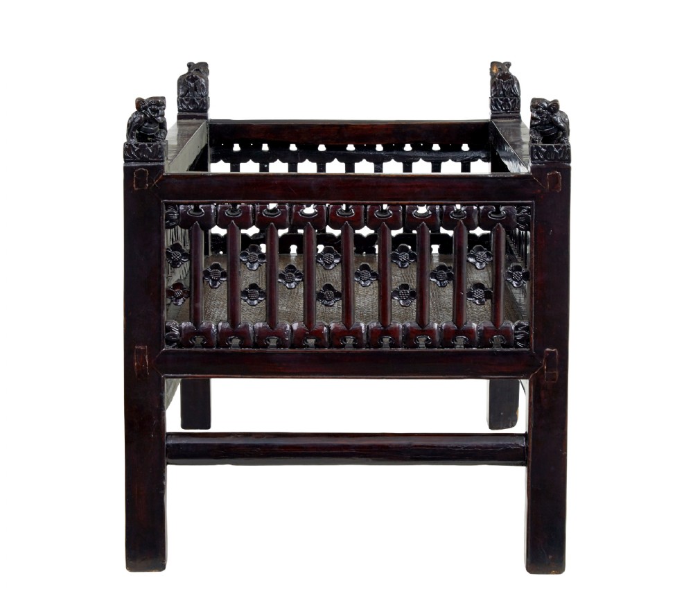 A 19th-century dark lacquered Chinese childs bed featuring carved lattice sides and guardian lion corner finials. View V