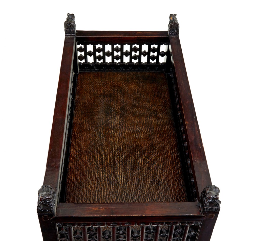 A 19th-century dark lacquered Chinese childs bed featuring carved lattice sides and guardian lion corner finials. View VI