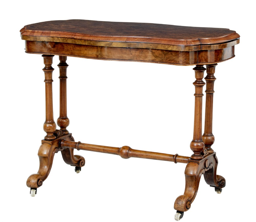A 19th-century Victorian walnut fold-over card table featuring turned dual pedestal legs, a central stretcher rail, scroll feet, and ceramic castors.