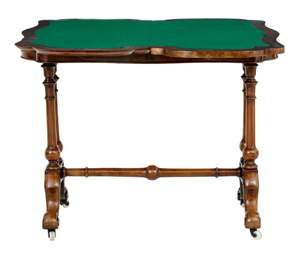 A 19th-century Victorian walnut fold-over card table featuring turned dual pedestal legs, a central stretcher rail, scroll feet, and ceramic castors. View VI