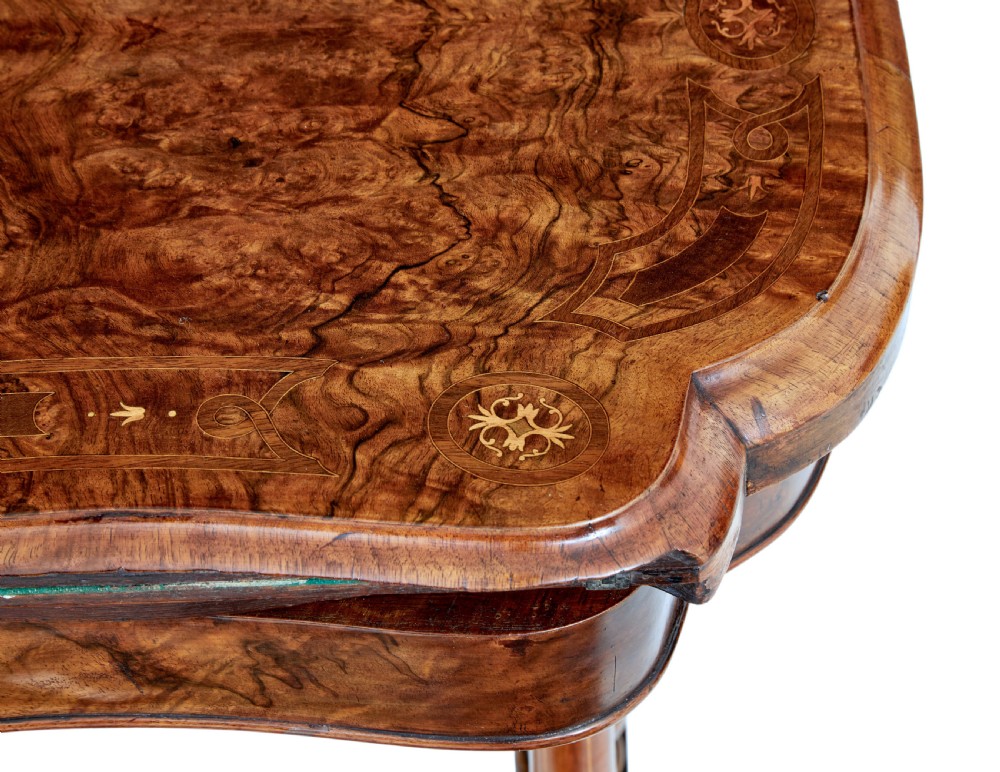 A 19th-century Victorian walnut fold-over card table featuring turned dual pedestal legs, a central stretcher rail, scroll feet, and ceramic castors. View X