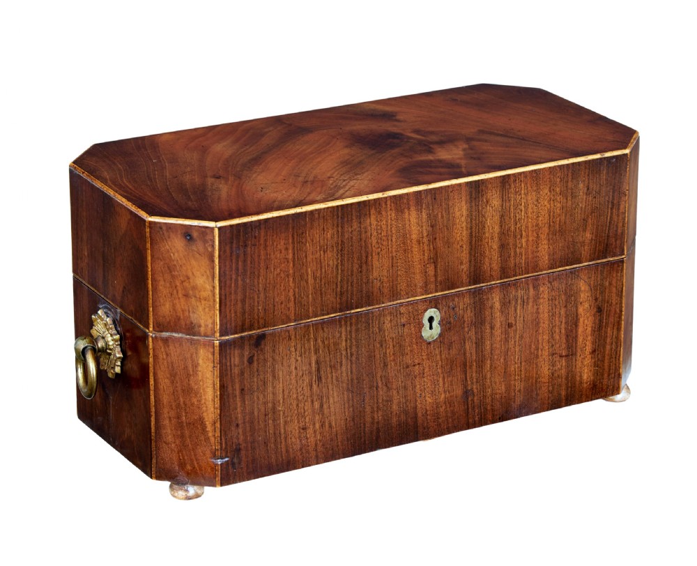 An early 19th-century mahogany tea caddy featuring a canted octagonal shape, brass side ring handles, a brass keyhole escutcheon, and bun feet.