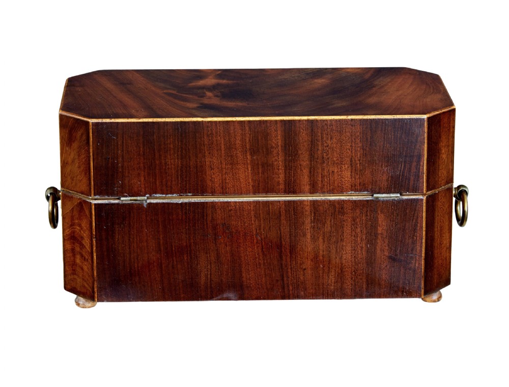 An early 19th-century mahogany tea caddy featuring a canted octagonal shape, brass side ring handles, a brass keyhole escutcheon, and bun feet. View V