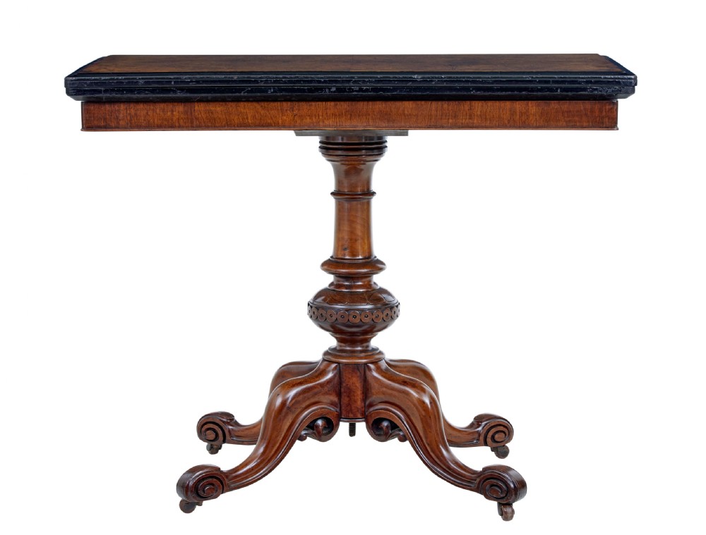 A 19th-century carved walnut fold-over card table featuring an ebonised top edge, a turned central stem, and four carved scroll feet with castors.