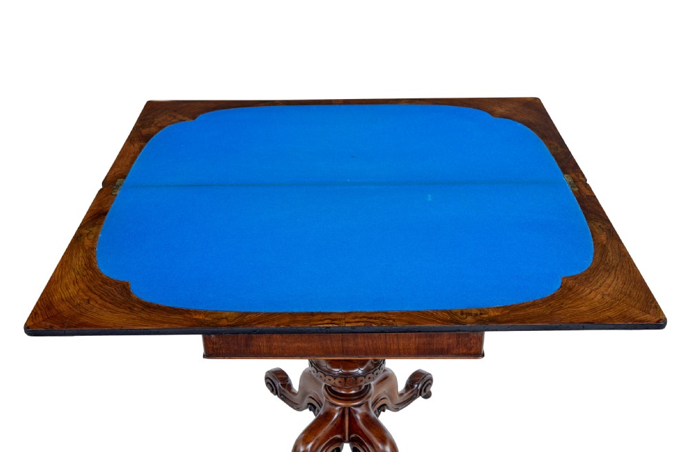A 19th-century carved walnut fold-over card table featuring an ebonised top edge, a turned central stem, and four carved scroll feet with castors. View V