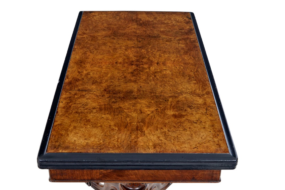 A 19th-century carved walnut fold-over card table featuring an ebonised top edge, a turned central stem, and four carved scroll feet with castors. View VII