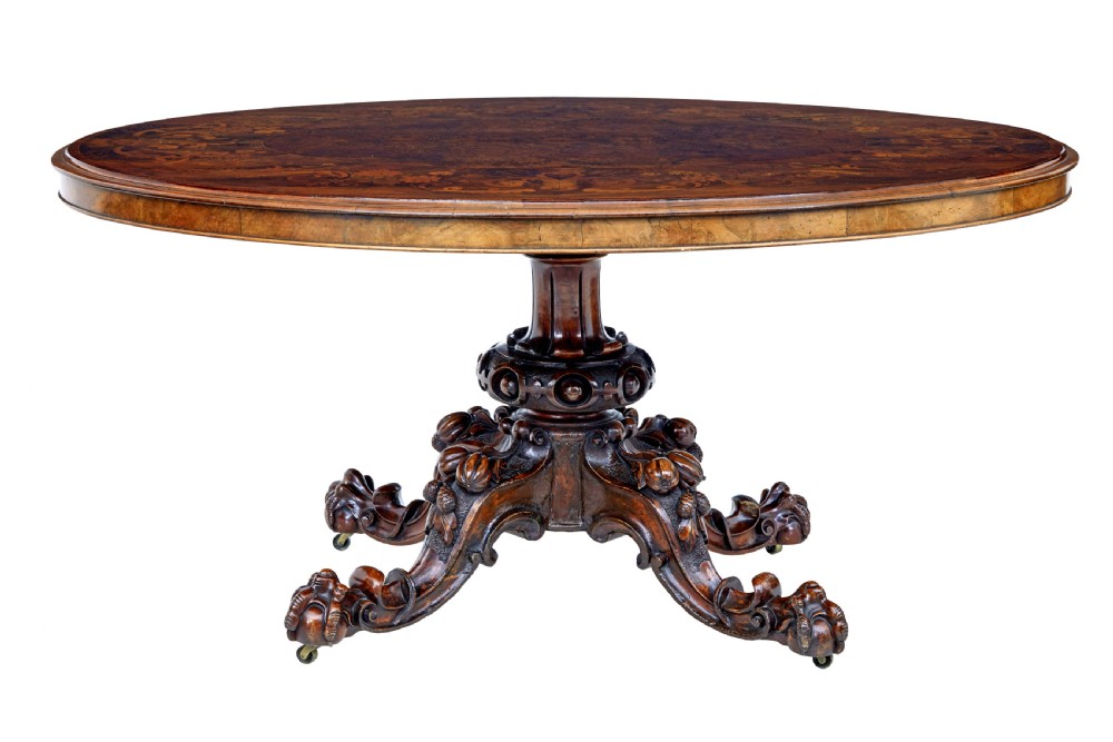 A 19th-century oval walnut tilt-top table with intricate floral marquetry inlay and a carved pedestal base with brass castors.
