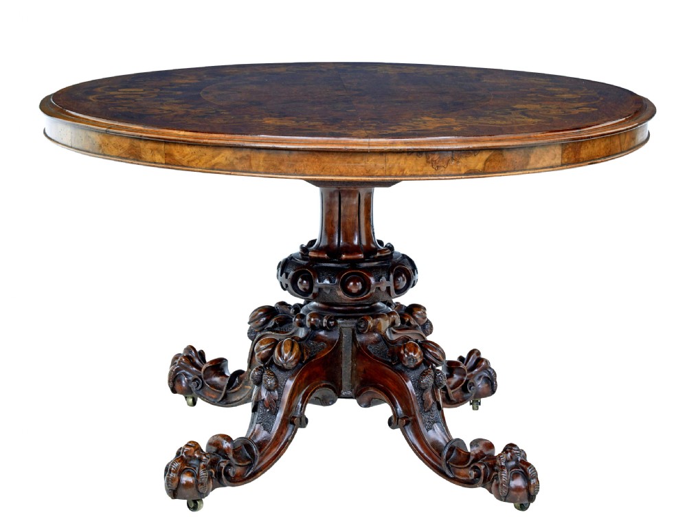 A 19th-century oval walnut tilt-top table with intricate floral marquetry inlay and a carved pedestal base with brass castors. View II