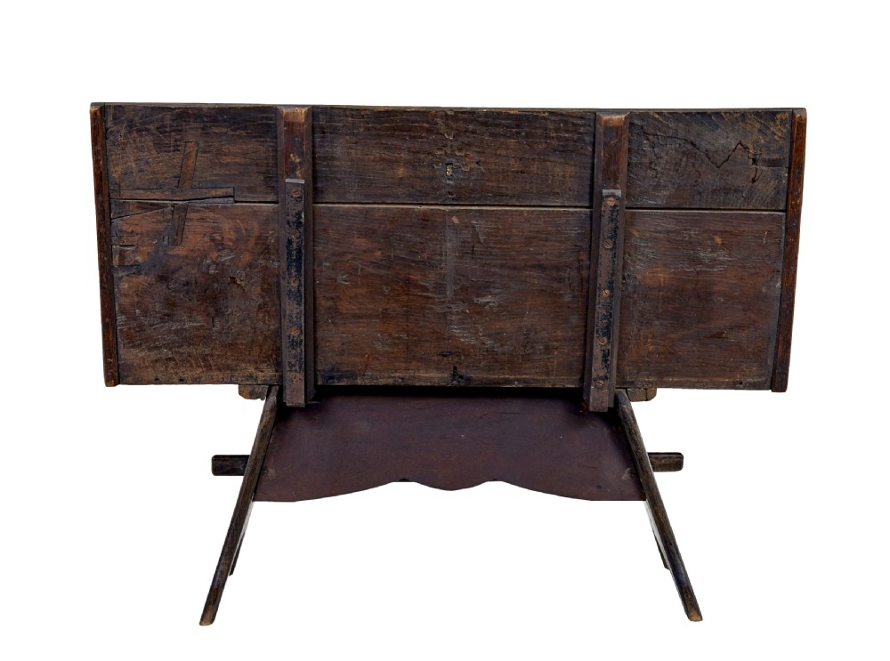 A dark carved oak bench featuring a high panelled back with intricate relief carvings and splayed trestle legs. View IV