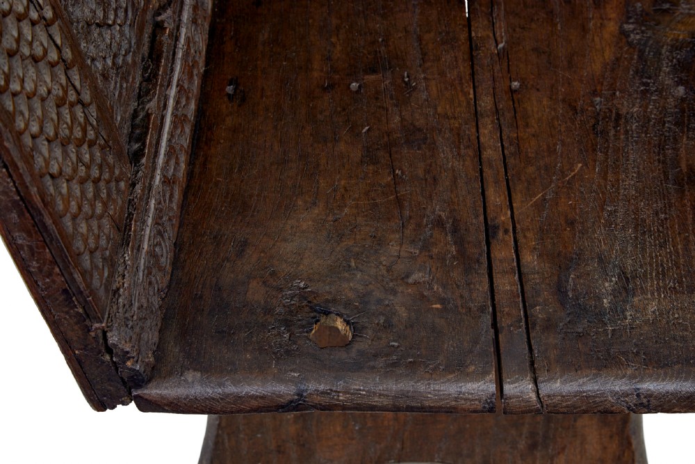 A dark carved oak bench featuring a high panelled back with intricate relief carvings and splayed trestle legs. View VII