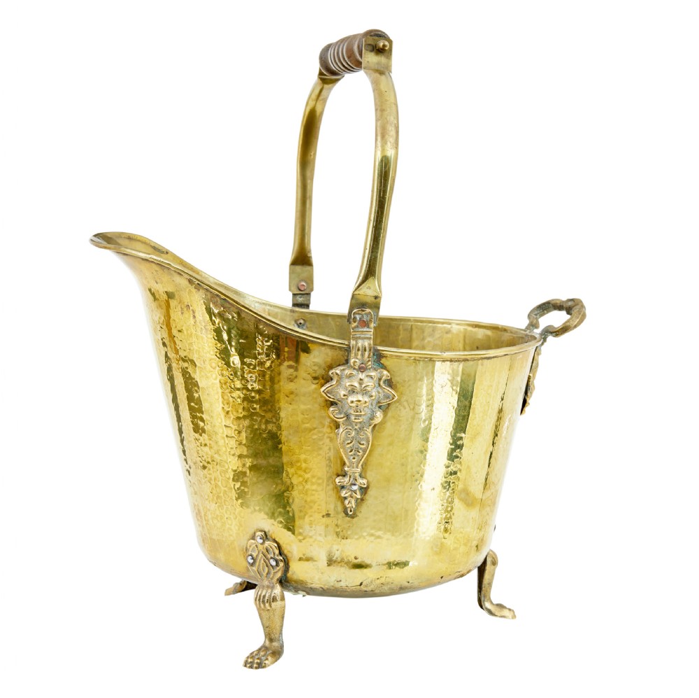 A 19th-century hammered brass helmet coal scuttle with an overhead handle, ornate side mounts, and paw feet. View II