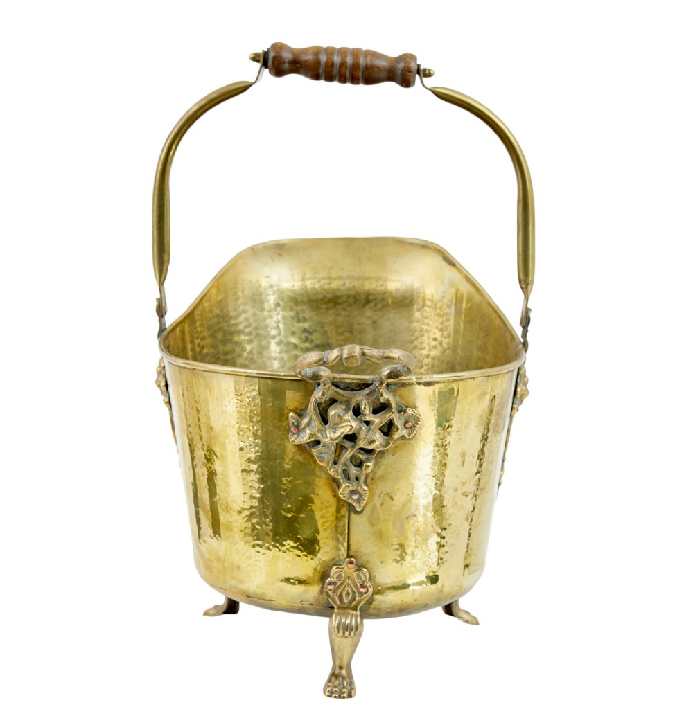 A 19th-century hammered brass helmet coal scuttle with an overhead handle, ornate side mounts, and paw feet. View IV