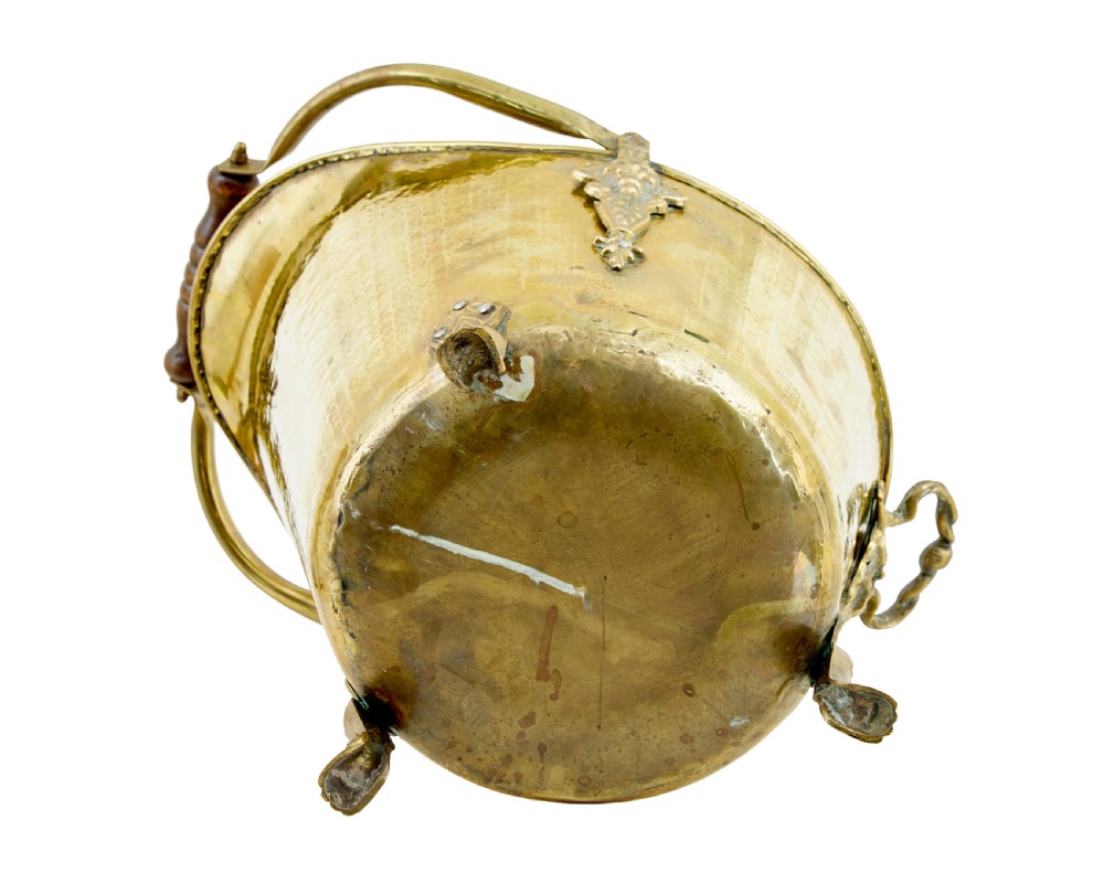 A 19th-century hammered brass helmet coal scuttle with an overhead handle, ornate side mounts, and paw feet. View VI