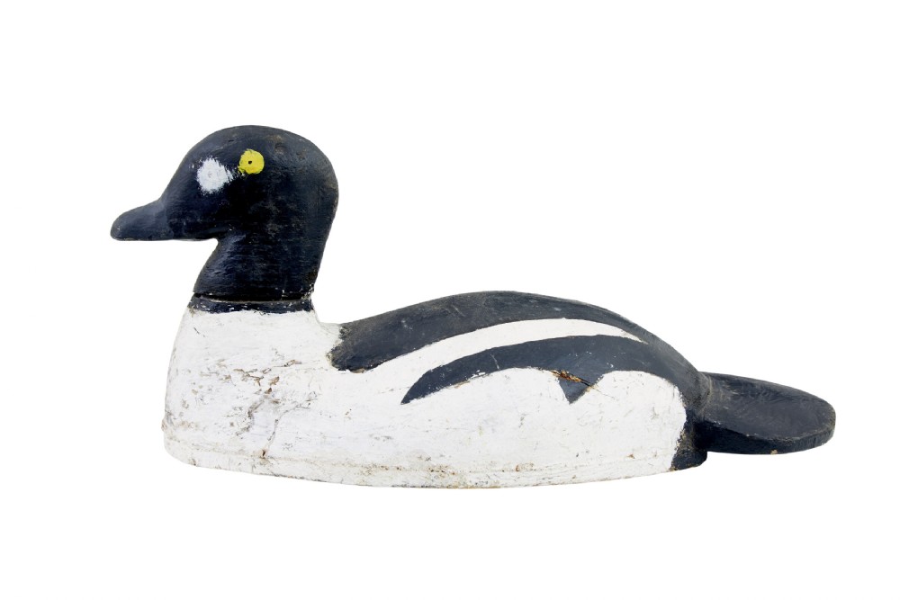 A hand-carved early 20th-century wooden duck decoy styled with distressed black and white painted finish and yellow eye detail.