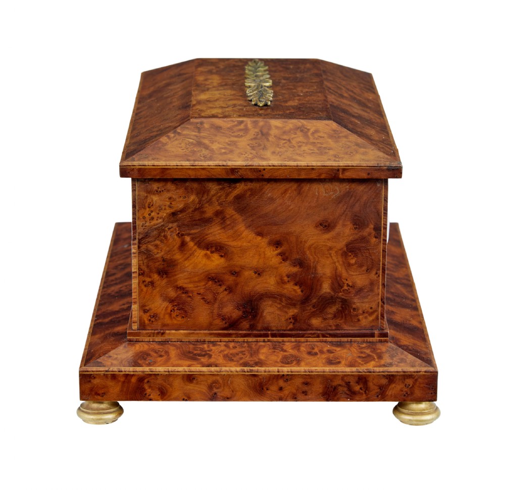 An early 20th-century burr yew desktop box featuring a circular clock face on the front, gilt brass top ornamentation, and brass feet. View V