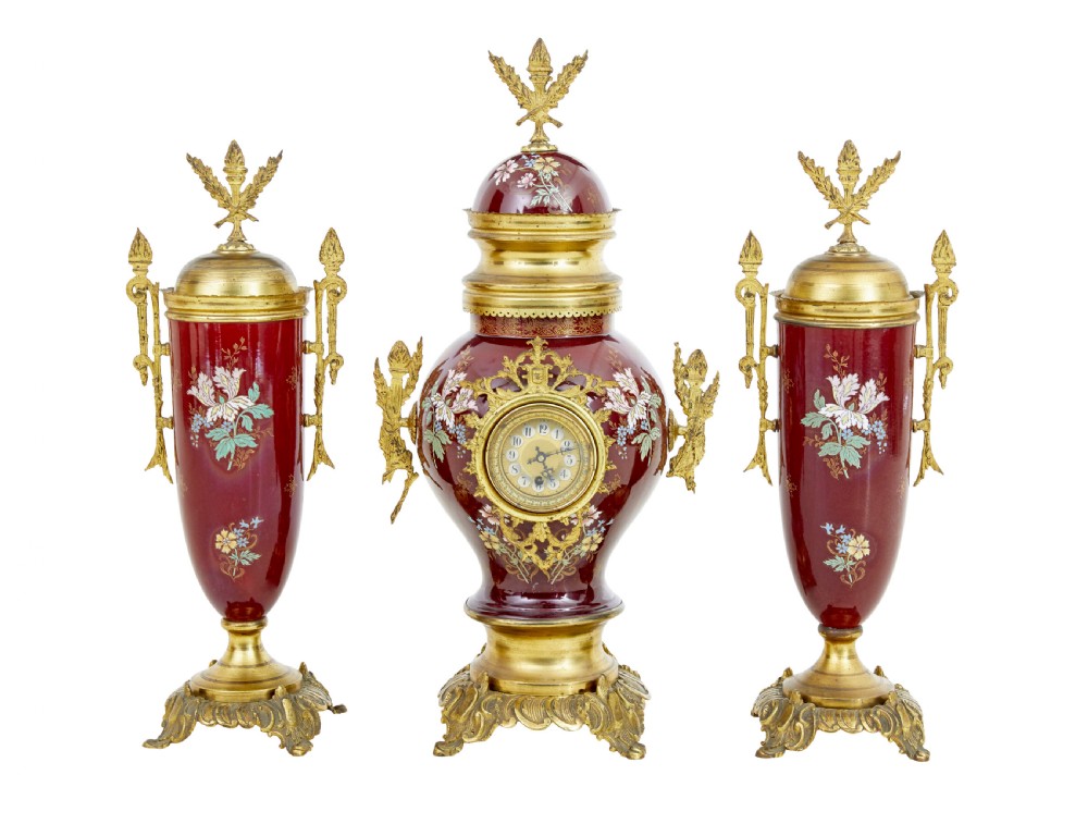 A nineteenth-century three-piece French toleware garniture set comprising a central clock urn and two matching side urns in crimson with hand-painted flowers and gilt mounts.