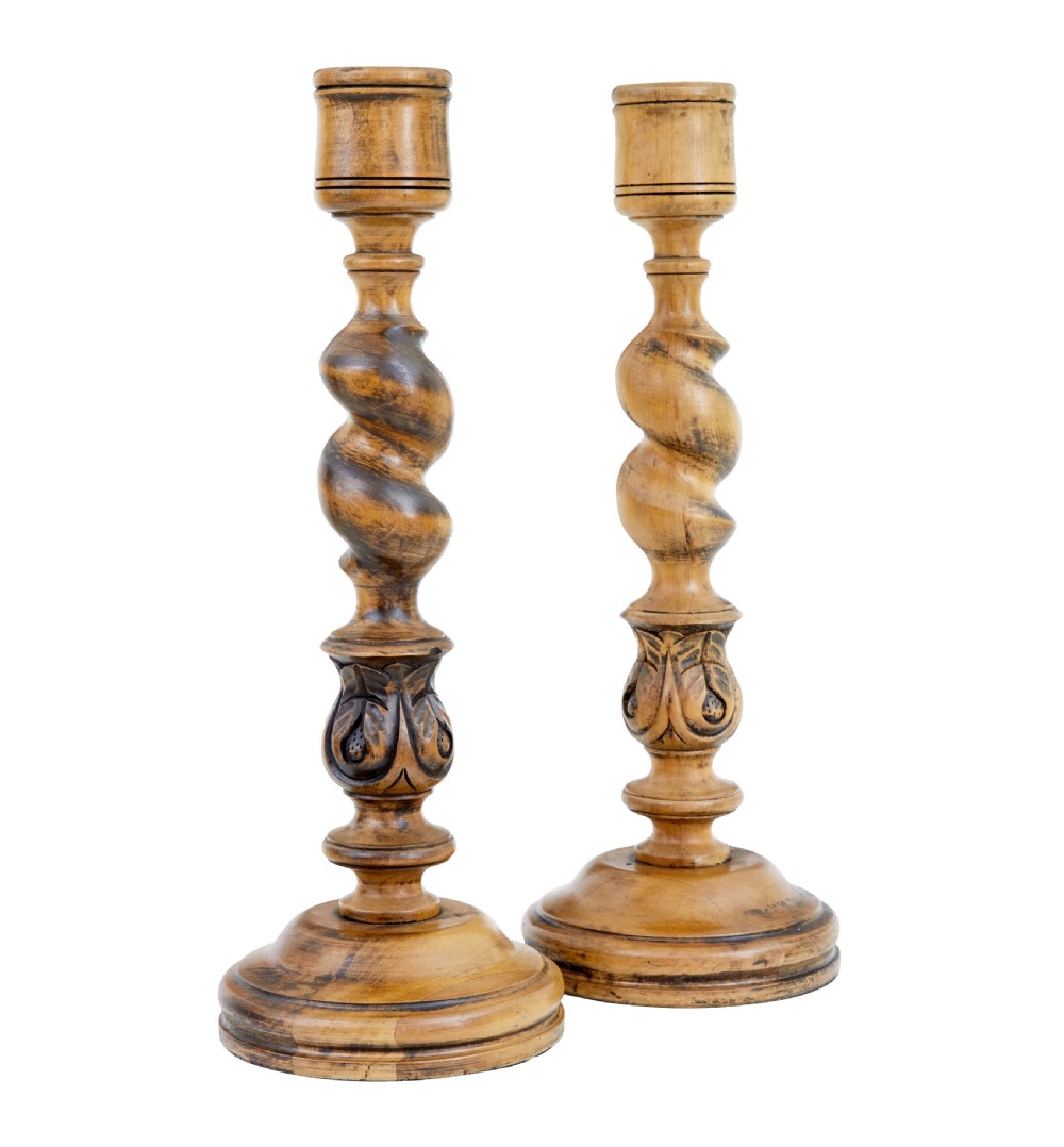 A pair of early 20th-century turned wood candlesticks featuring spiral stems, carved leaf accents, and wide circular bases.