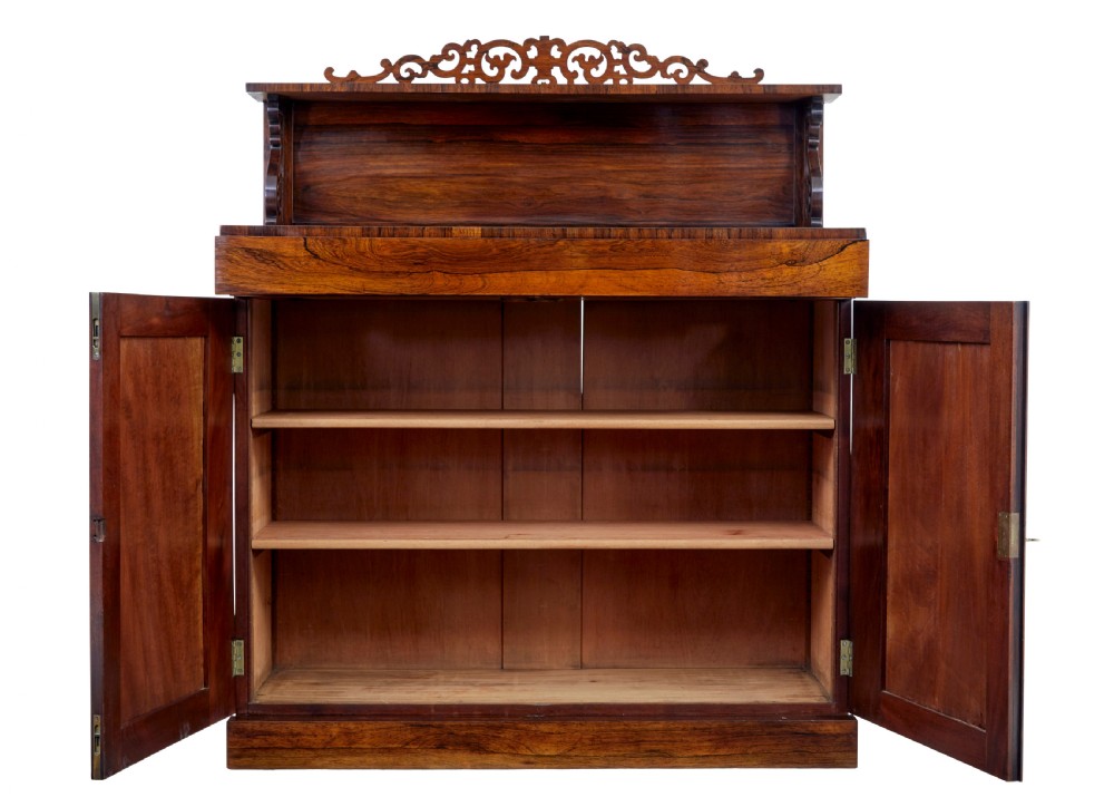 A nineteenth-century Regency palisander chiffonier sideboard with its two panelled doors open, revealing internal wooden shelves, topped with a carved scrollwork gallery shelf.