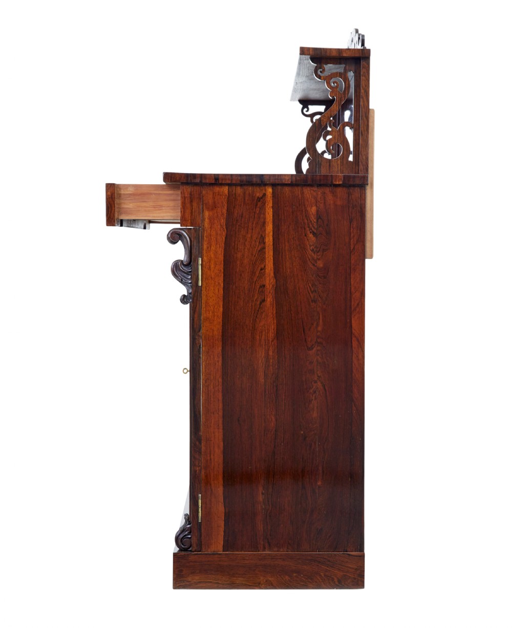 A nineteenth-century Regency palisander chiffonier sideboard with its two panelled doors open, revealing internal wooden shelves, topped with a carved scrollwork gallery shelf. View III