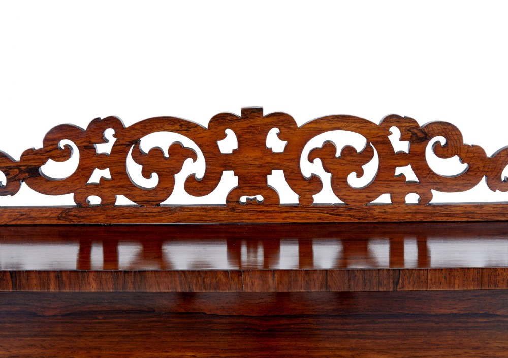 A nineteenth-century Regency palisander chiffonier sideboard with its two panelled doors open, revealing internal wooden shelves, topped with a carved scrollwork gallery shelf. View VII