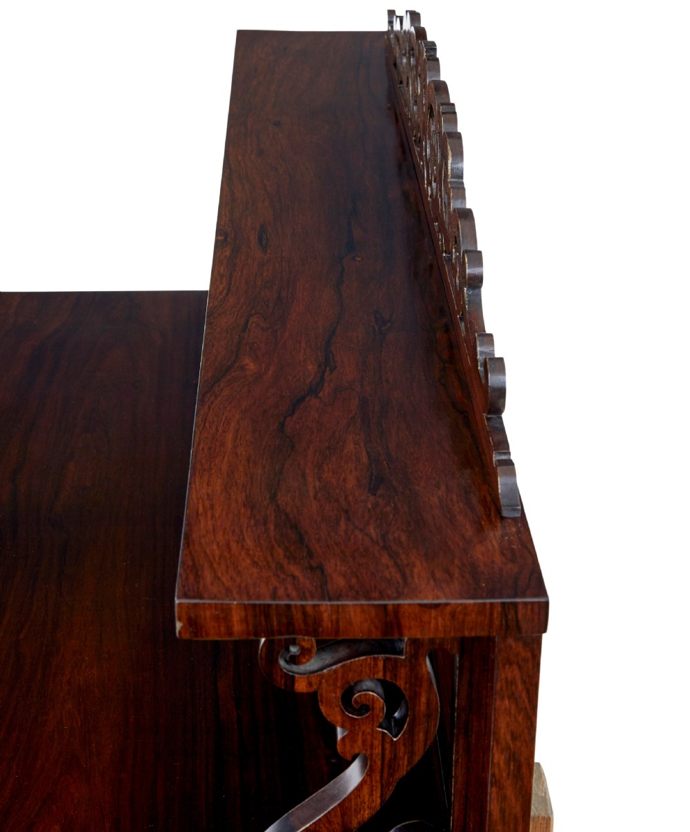 A nineteenth-century Regency palisander chiffonier sideboard with its two panelled doors open, revealing internal wooden shelves, topped with a carved scrollwork gallery shelf. View IX