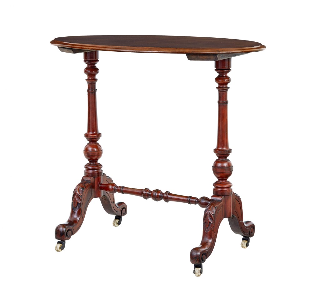A 19th-century Victorian oval occasional table in polished walnut featuring twin turned support columns, carved legs, a central stretcher, and ceramic castors.