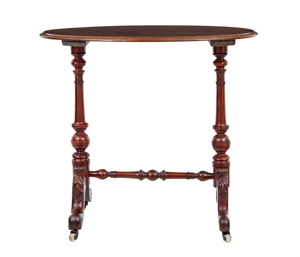 A 19th-century Victorian oval occasional table in polished walnut featuring twin turned support columns, carved legs, a central stretcher, and ceramic castors. View II