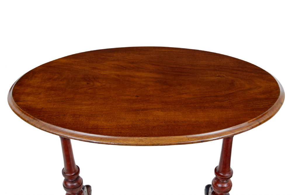 A 19th-century Victorian oval occasional table in polished walnut featuring twin turned support columns, carved legs, a central stretcher, and ceramic castors. View VI