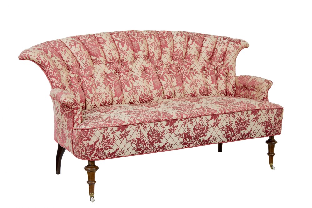 An early 20th century three-piece upholstered salon suite featuring a two-seater settee and two matching armchairs with pink and cream floral damask pattern, button-tufted fluted backs, and turned wooden legs with brass castors. View III
