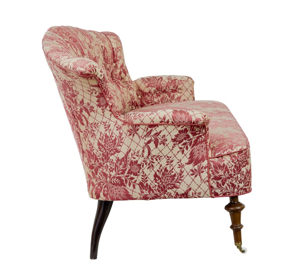 An early 20th century three-piece upholstered salon suite featuring a two-seater settee and two matching armchairs with pink and cream floral damask pattern, button-tufted fluted backs, and turned wooden legs with brass castors. View IV