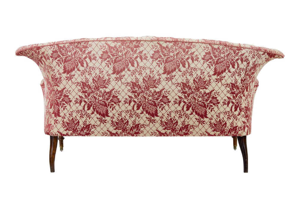 An early 20th century three-piece upholstered salon suite featuring a two-seater settee and two matching armchairs with pink and cream floral damask pattern, button-tufted fluted backs, and turned wooden legs with brass castors. View V